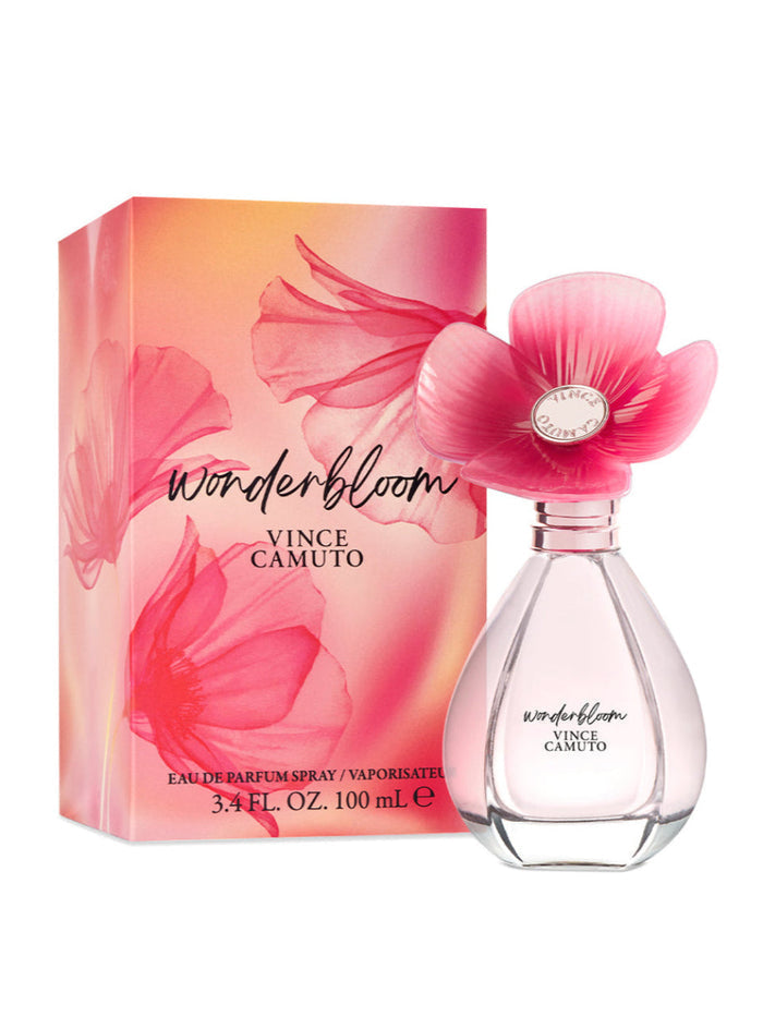 A 3.4 oz bottle of Vince Camuto Wonderbloom Eau de Parfum Spray, featuring a clear, elegant design with a pink flower-shaped cap, is displayed next to its coordinating pink floral-patterned box. This enchanting fragrance captures the essence of white freesia and refreshing pear leaves for a truly captivating scent experience.